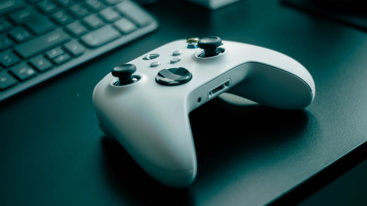 Mando Xbox inalámbrico blanco sobre un escritorio oscuro, con teclado difuminado al fondo