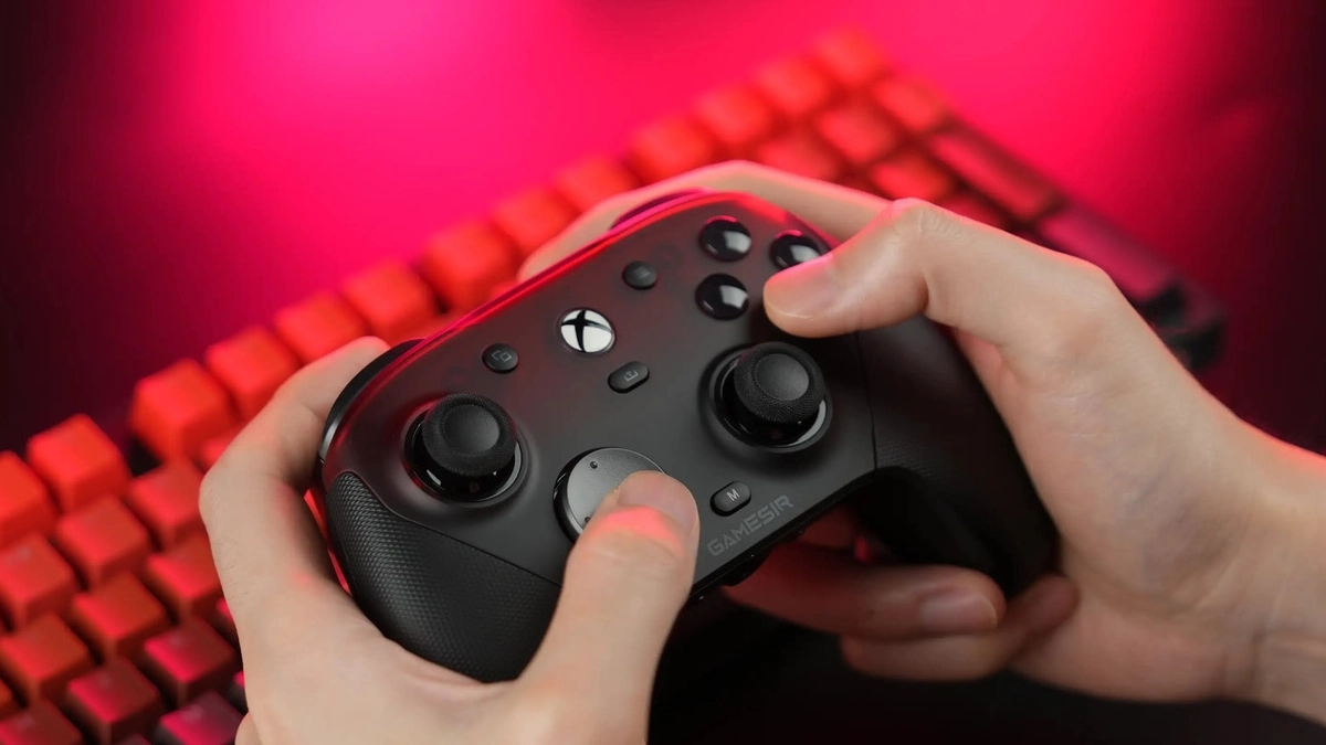 Manos sujetando un mando GameSir negro frente a un teclado con luz roja