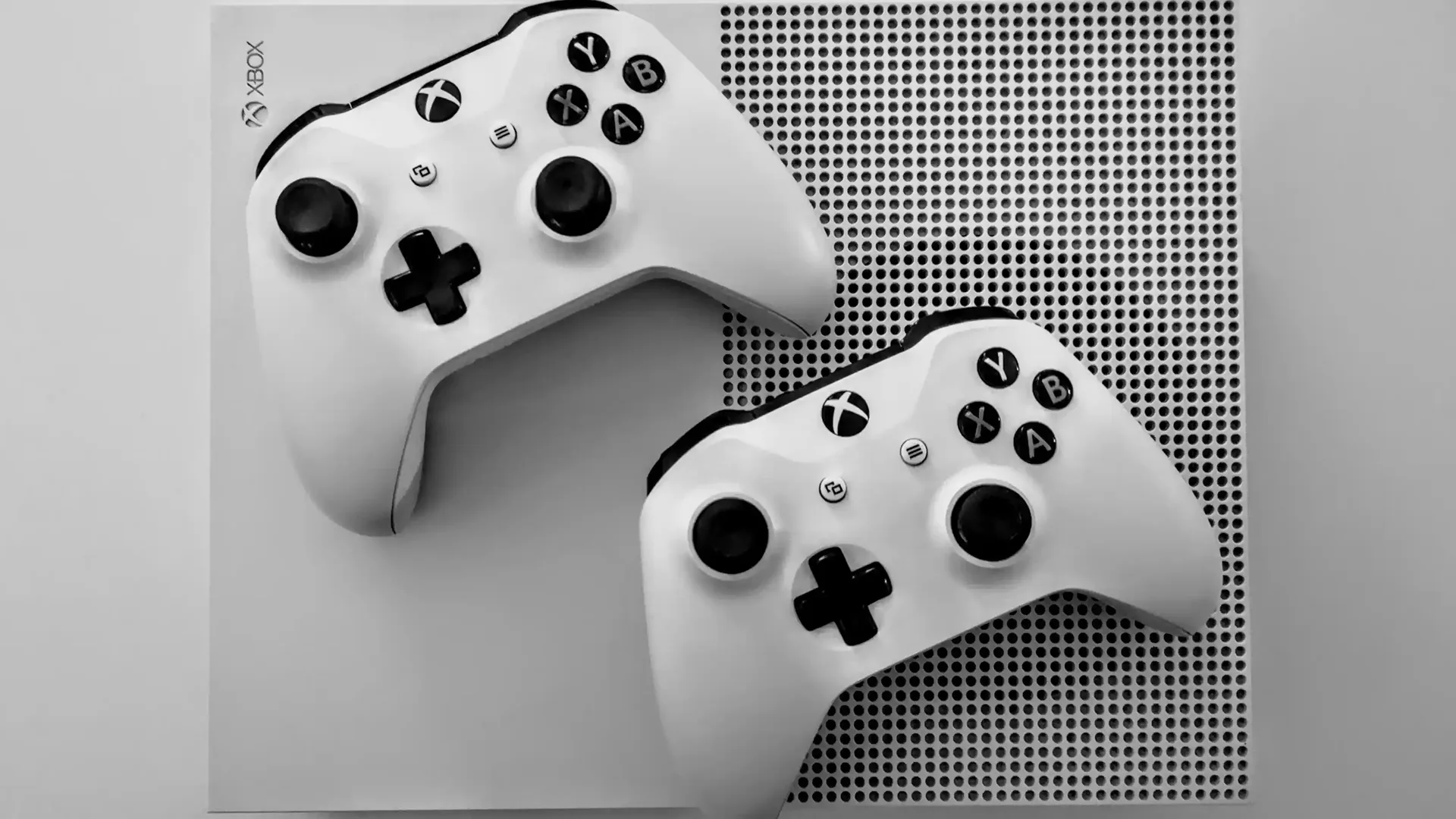 Consola Xbox con dos mandos encima, de color blanco